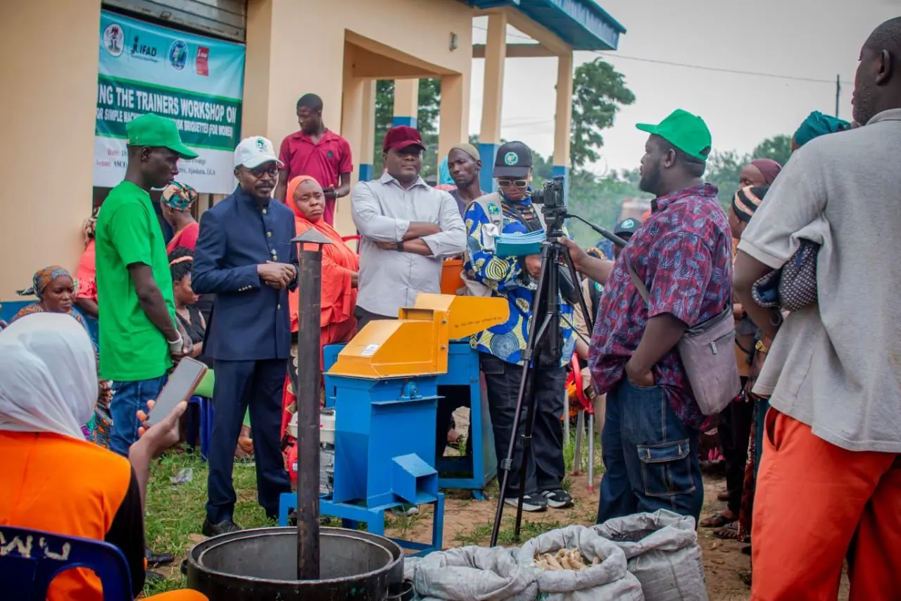 A crowd around a briquette press at an outdoor training workshop